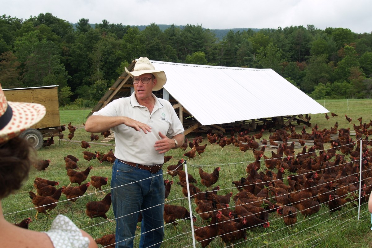 Joel Salatin standing among free-range hens and a portable coop on a pasture